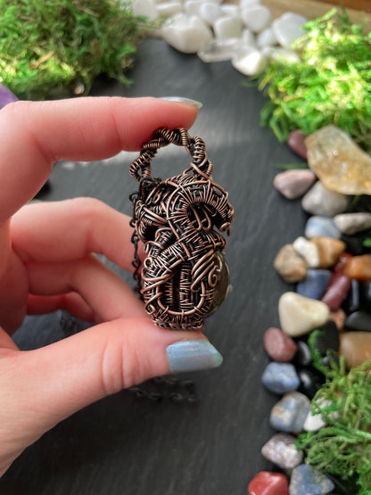 Copper amulet held between fingers with a natural stone background