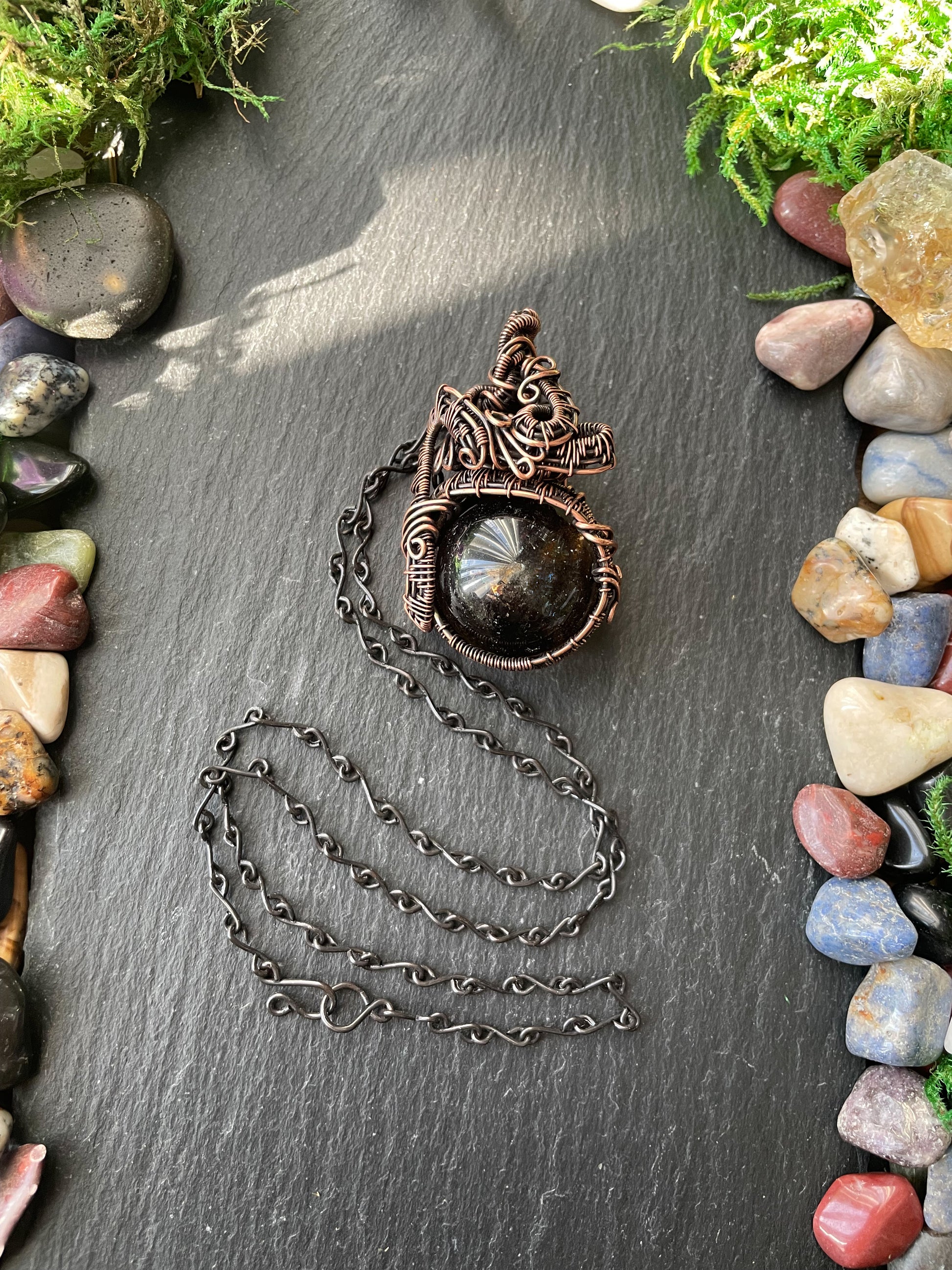 Necklace with a stone amulet on a dark surface surrounded by stones and moss
