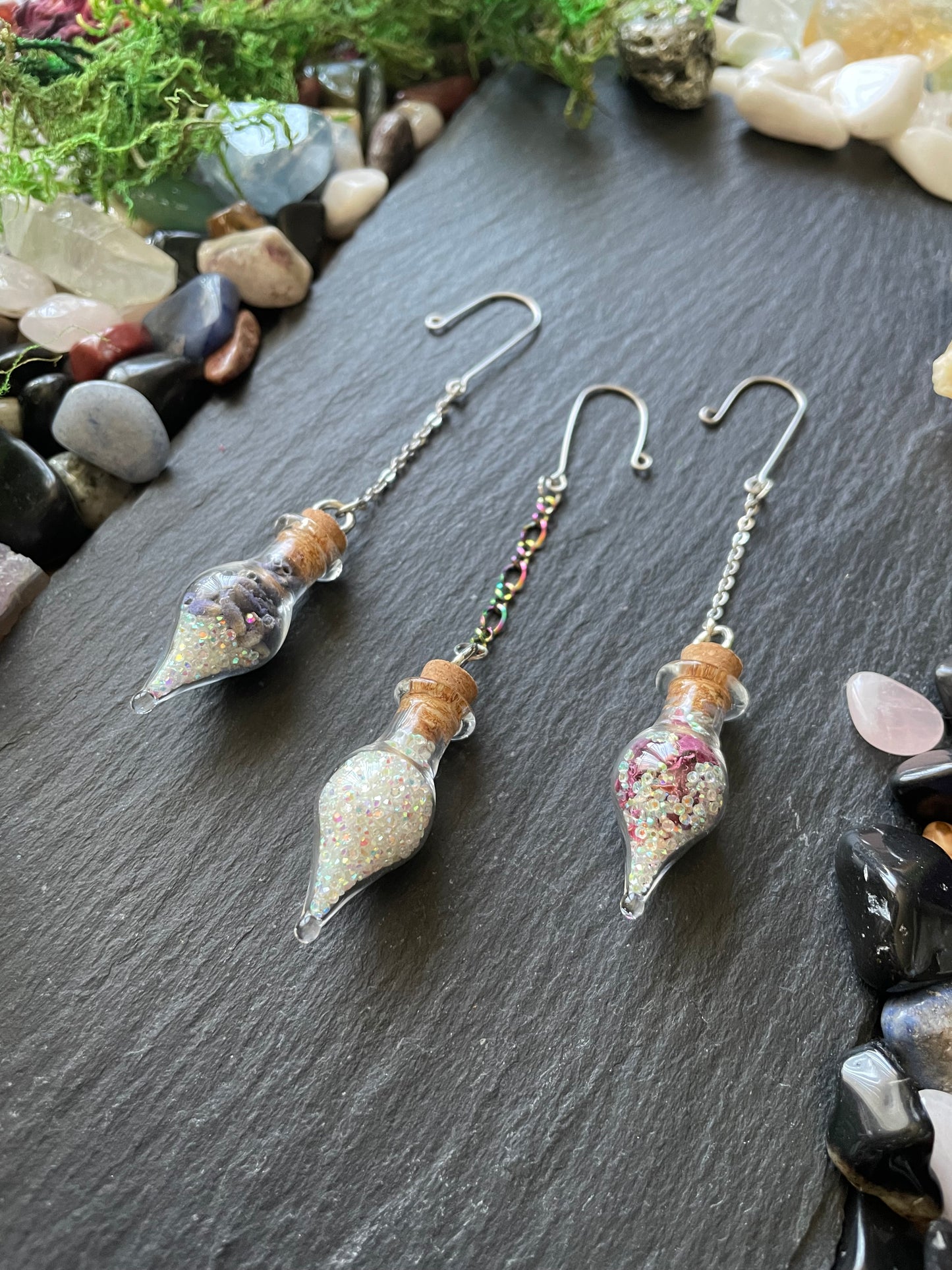 Plant charms on a dark surface with pebbles and moss.