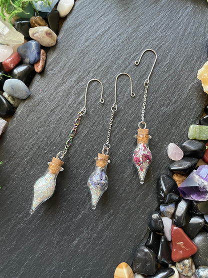 Plant charms with flowers and sparkles on a dark stone surface with small stones around