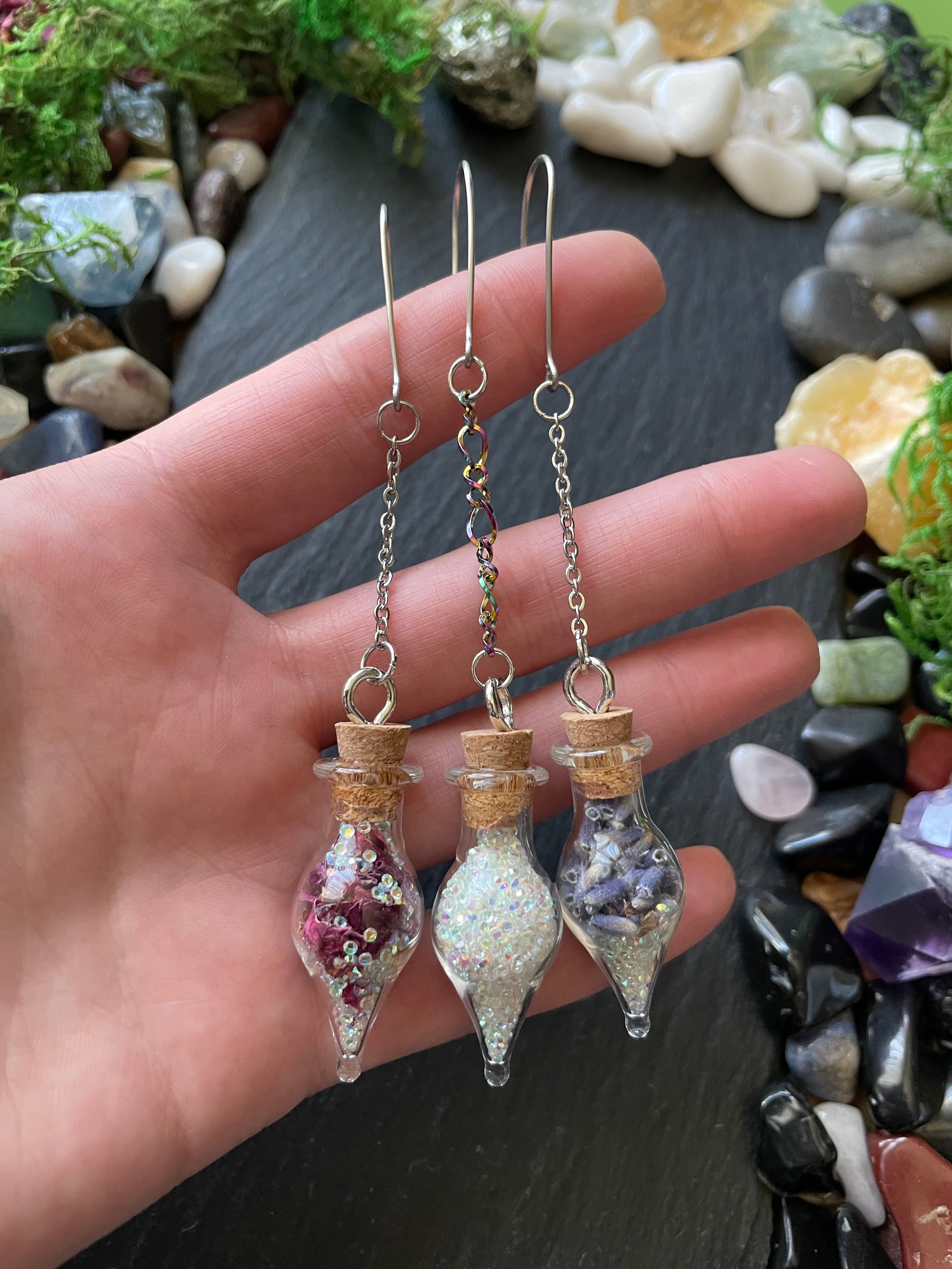 Hand holding three small glass vials with flowers inside against a stone background