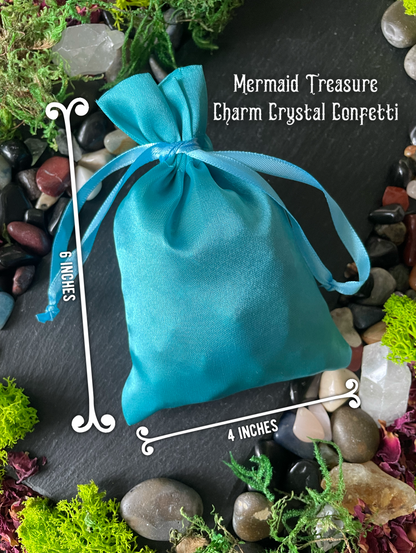 Blue drawstring bag labeled 'Mermaid Treasure Charm Crystal Confetti' on a stone and moss background.