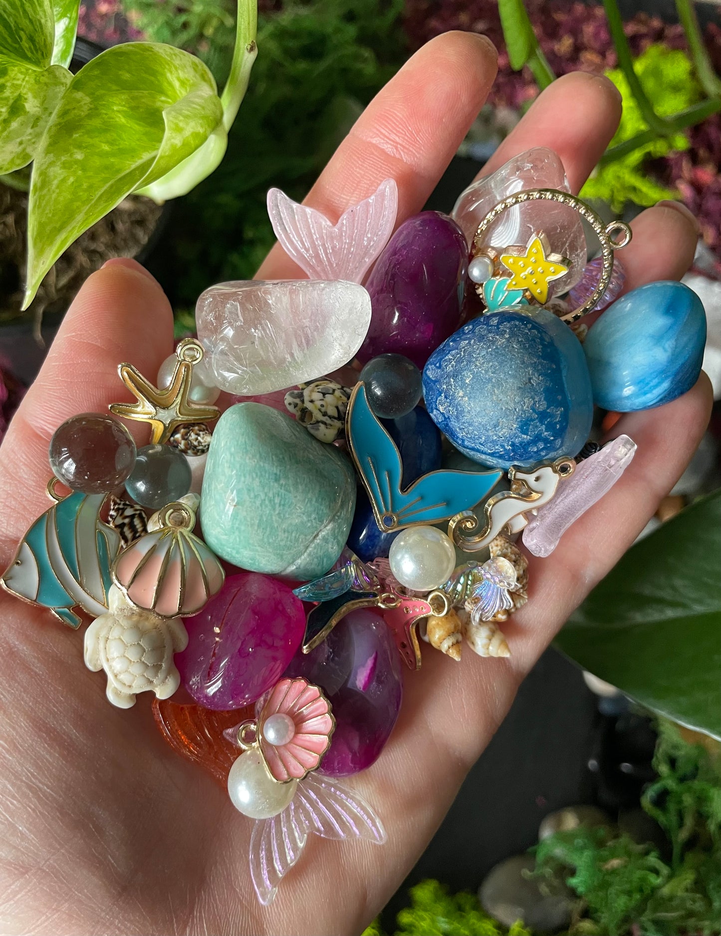Hand holding a collection of colorful jewelry charms against a natural background