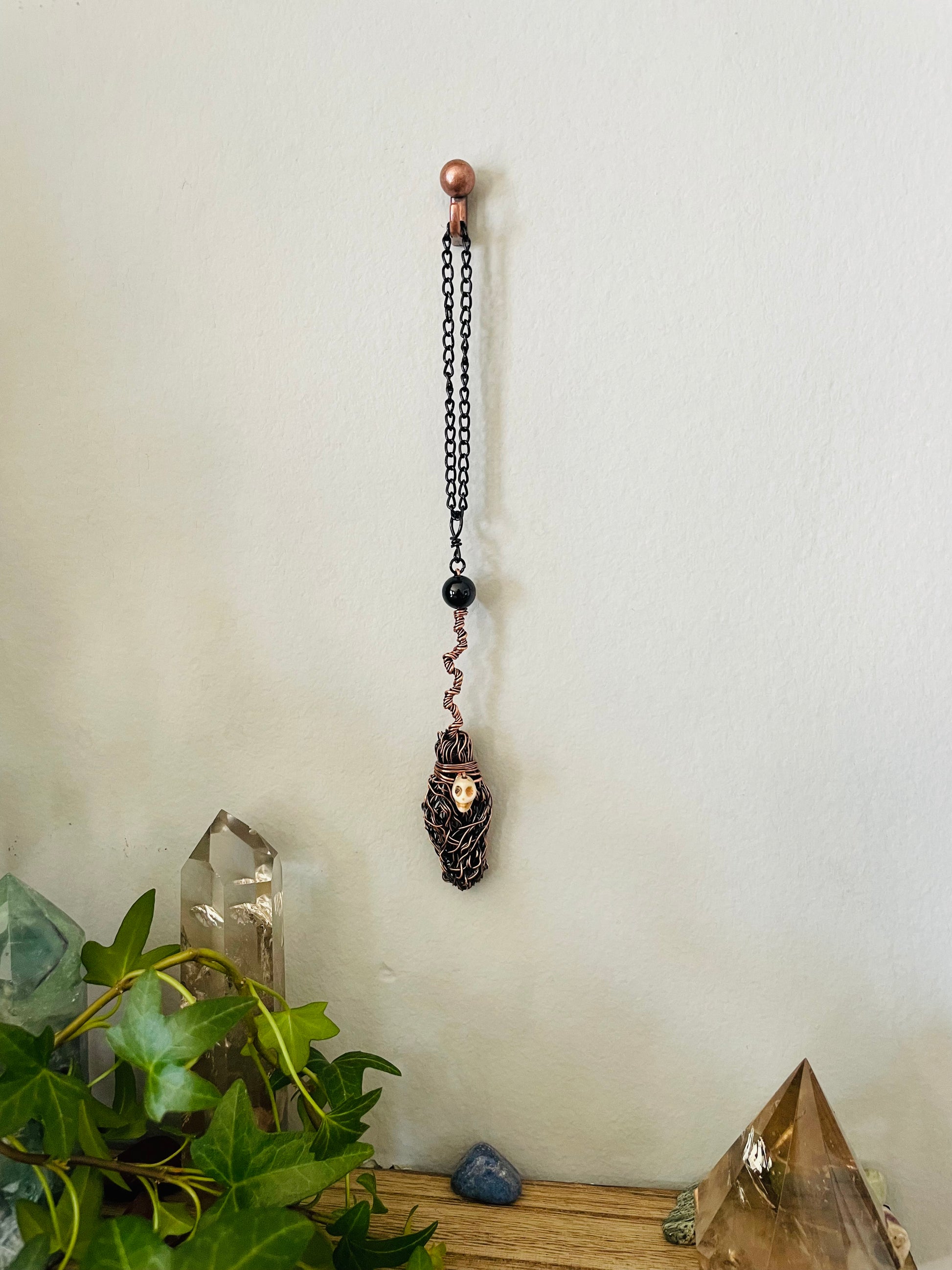 Decorative broom wall hanging with a skull design on a chain against a white wall.
