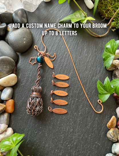Custom name charm for a broom on a dark surface with stones and leaves