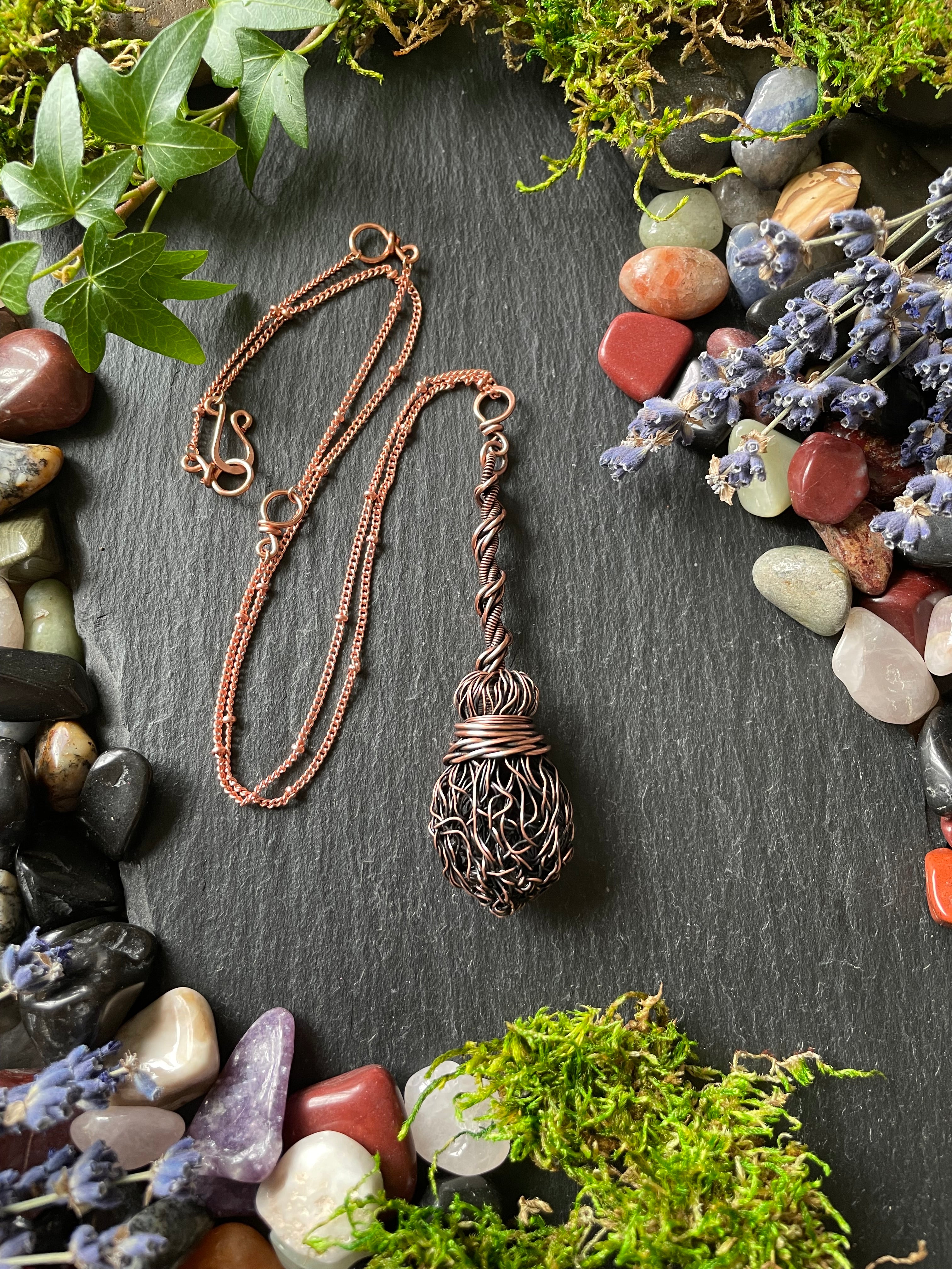 Miniature witch's broom made of copper wires, attached to a copper chain and placed on a stone slate for display