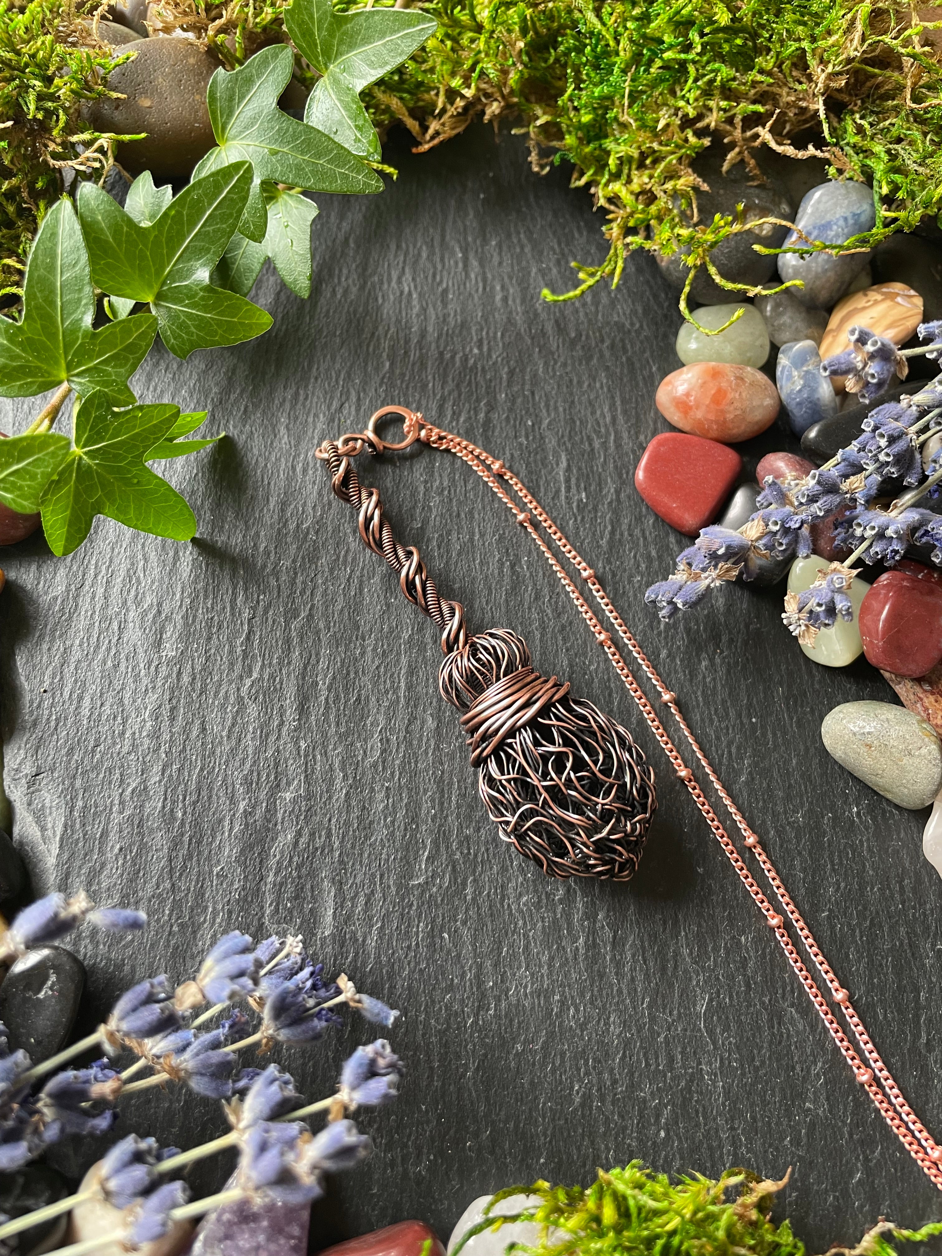 Miniature wire broom pendant attached to a copper chain, surrounded by gems, lavender, and plants