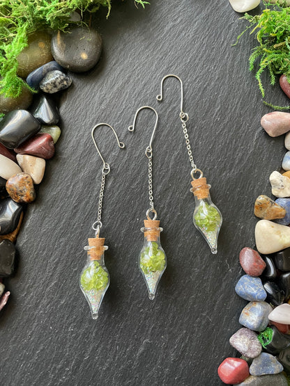 Glass vials with green crystals on a dark surface with stones and moss
