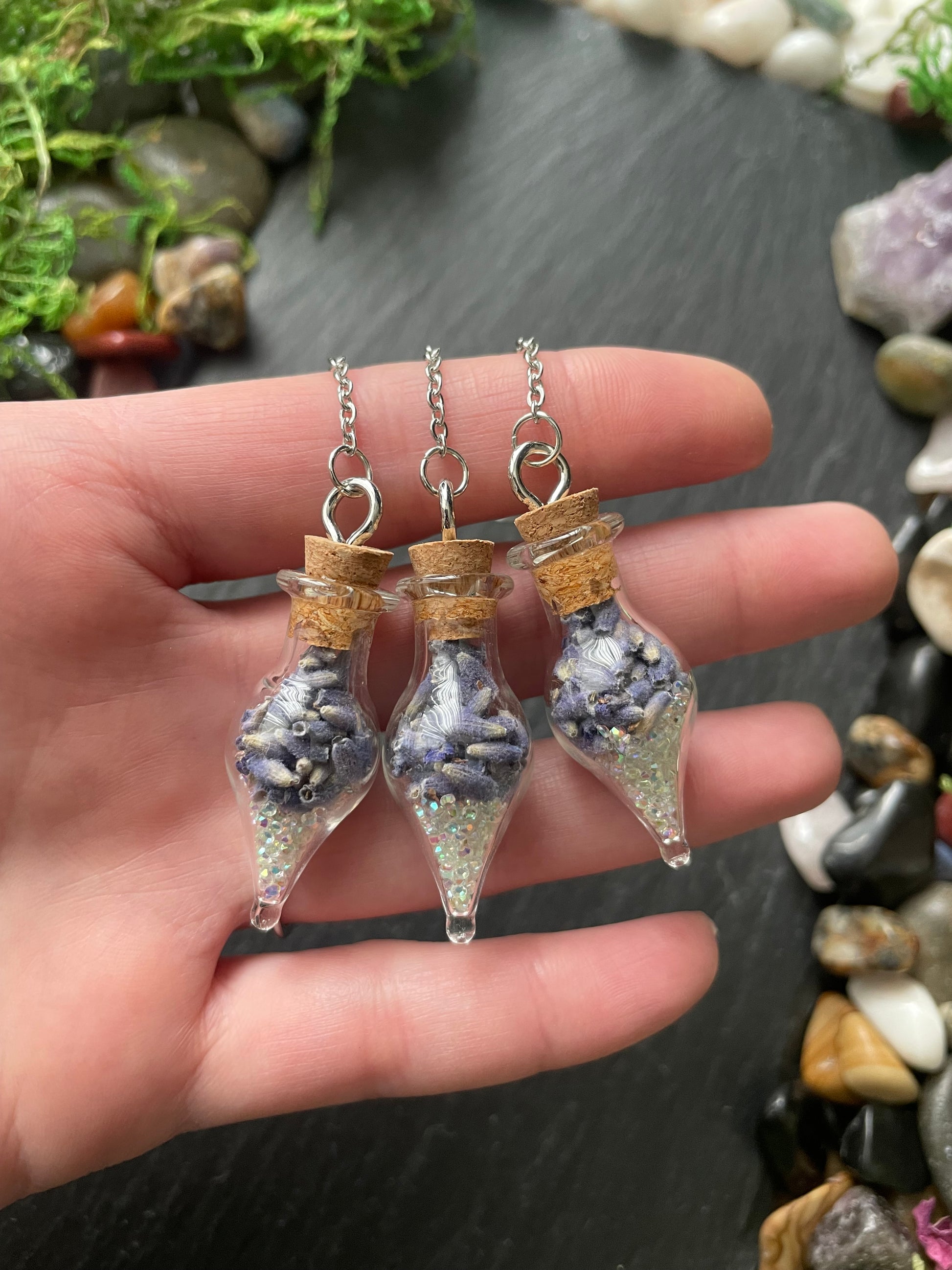 Hand holding three small glass vials with lavender flowers inside against a natural stone background