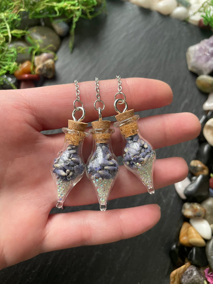 Hand holding three small glass vials with lavender flowers inside against a natural stone background