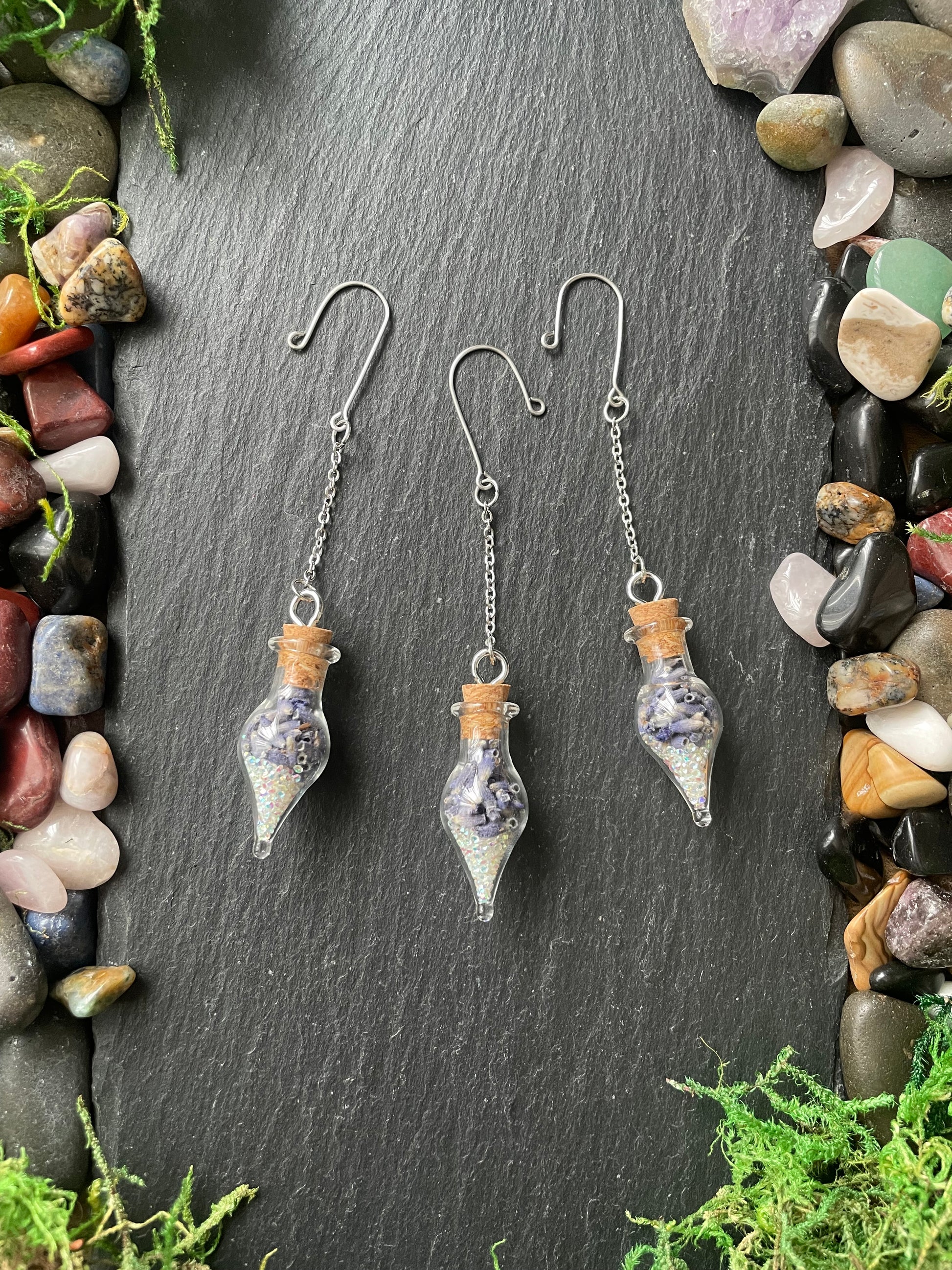 Glass bottle plant charms a dark stone surface with gemstones and greenery.