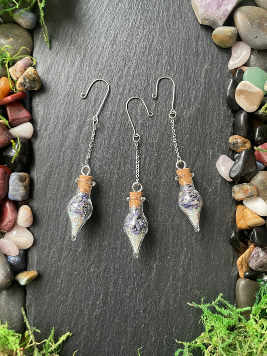 Glass bottle plant charms a dark stone surface with gemstones and greenery.