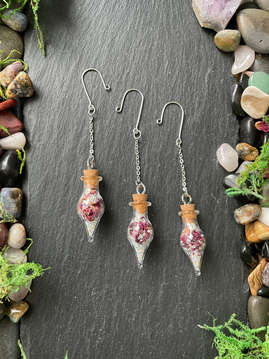 Three decorative plant charms with rose petals and crystals on a dark stone surface.