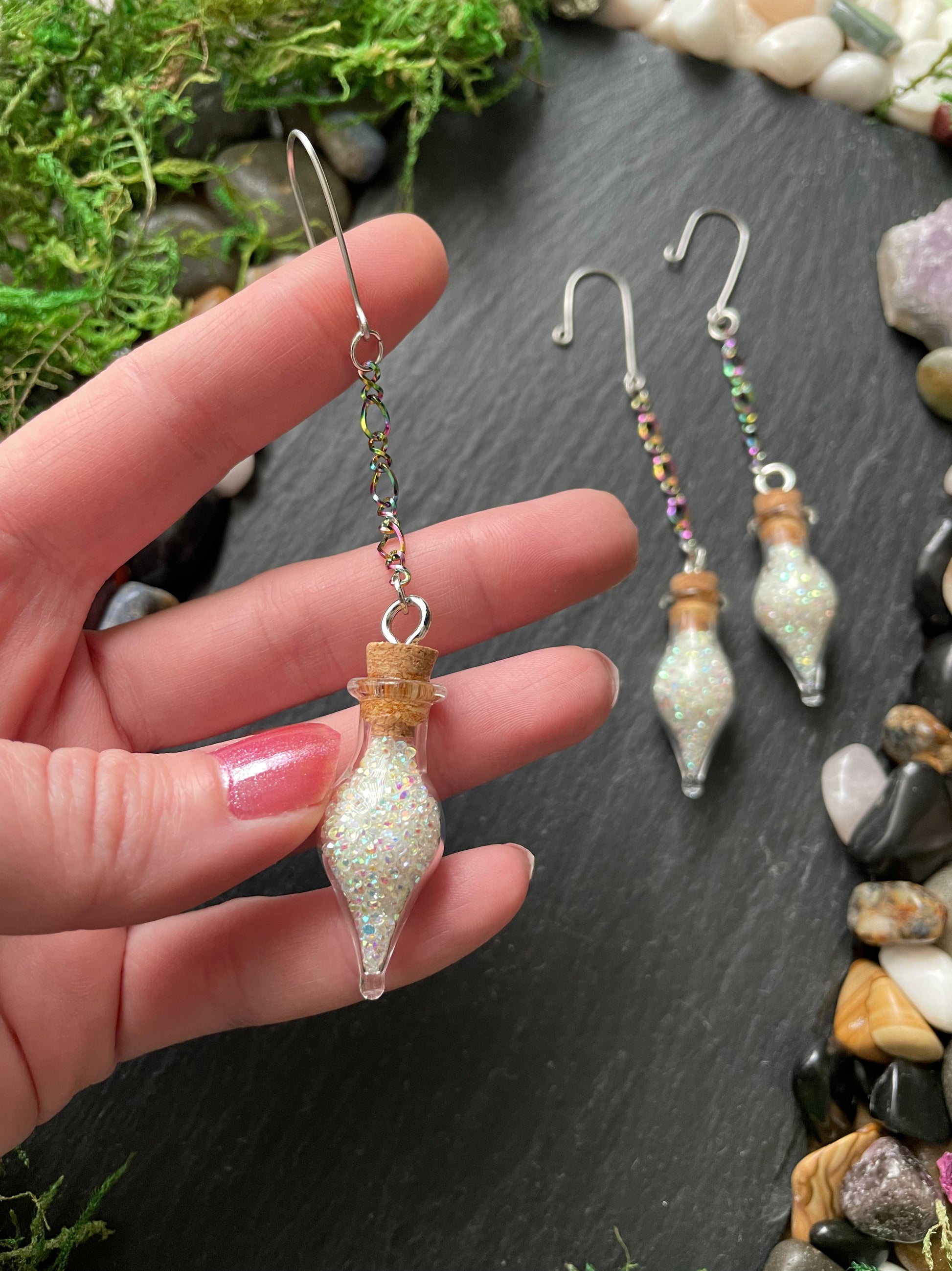 Hand holding a decorative charms with a small bottle-like design, set against a natural stone background.