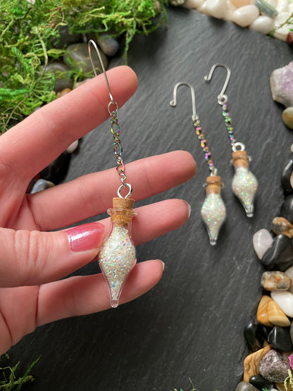 Hand holding a decorative charms with a small bottle-like design, set against a natural stone background.