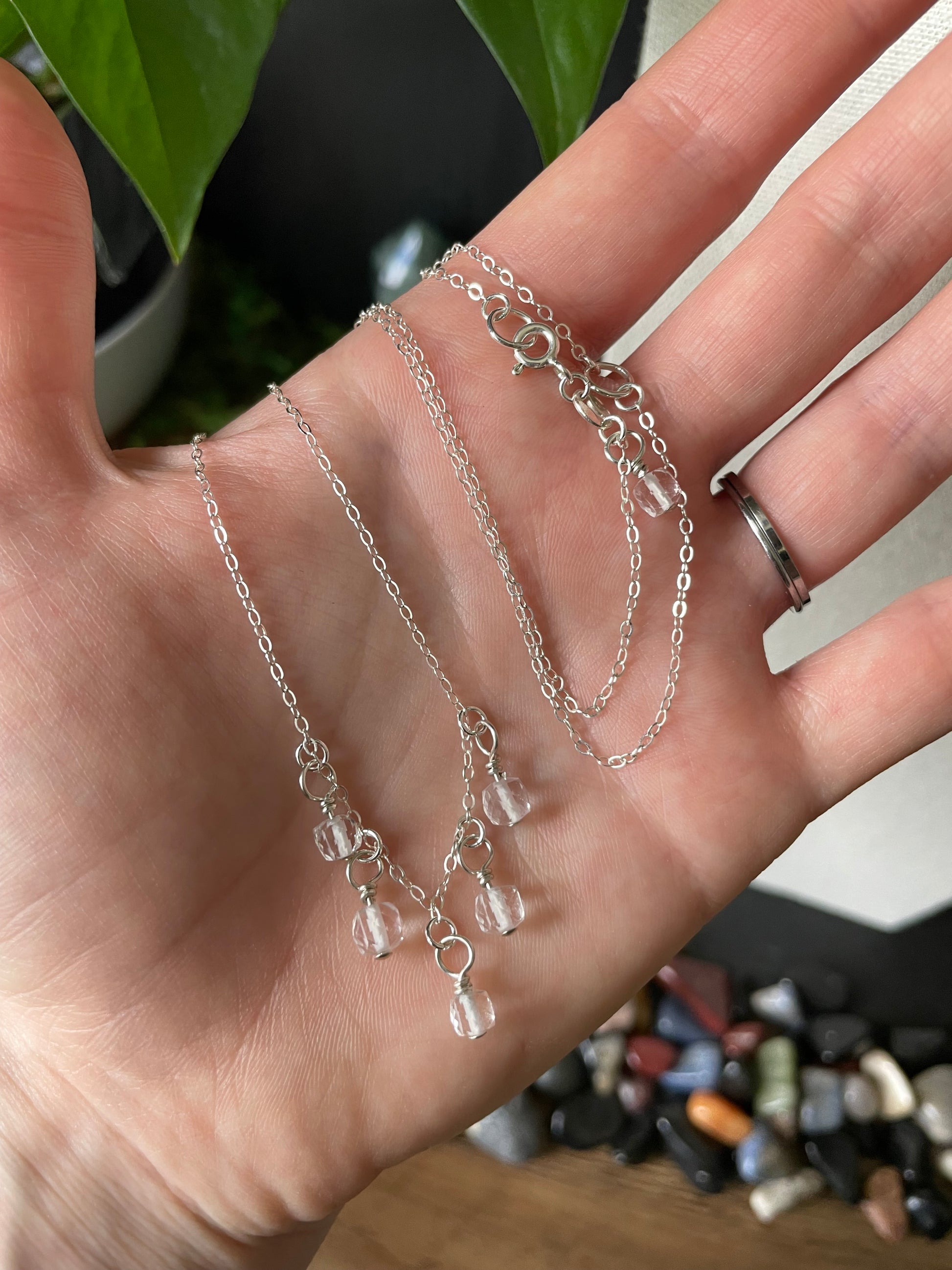 Silver necklace with charms held in a hand against a blurred background