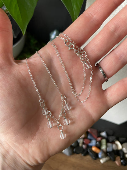 Silver necklace with charms held in a hand against a blurred background