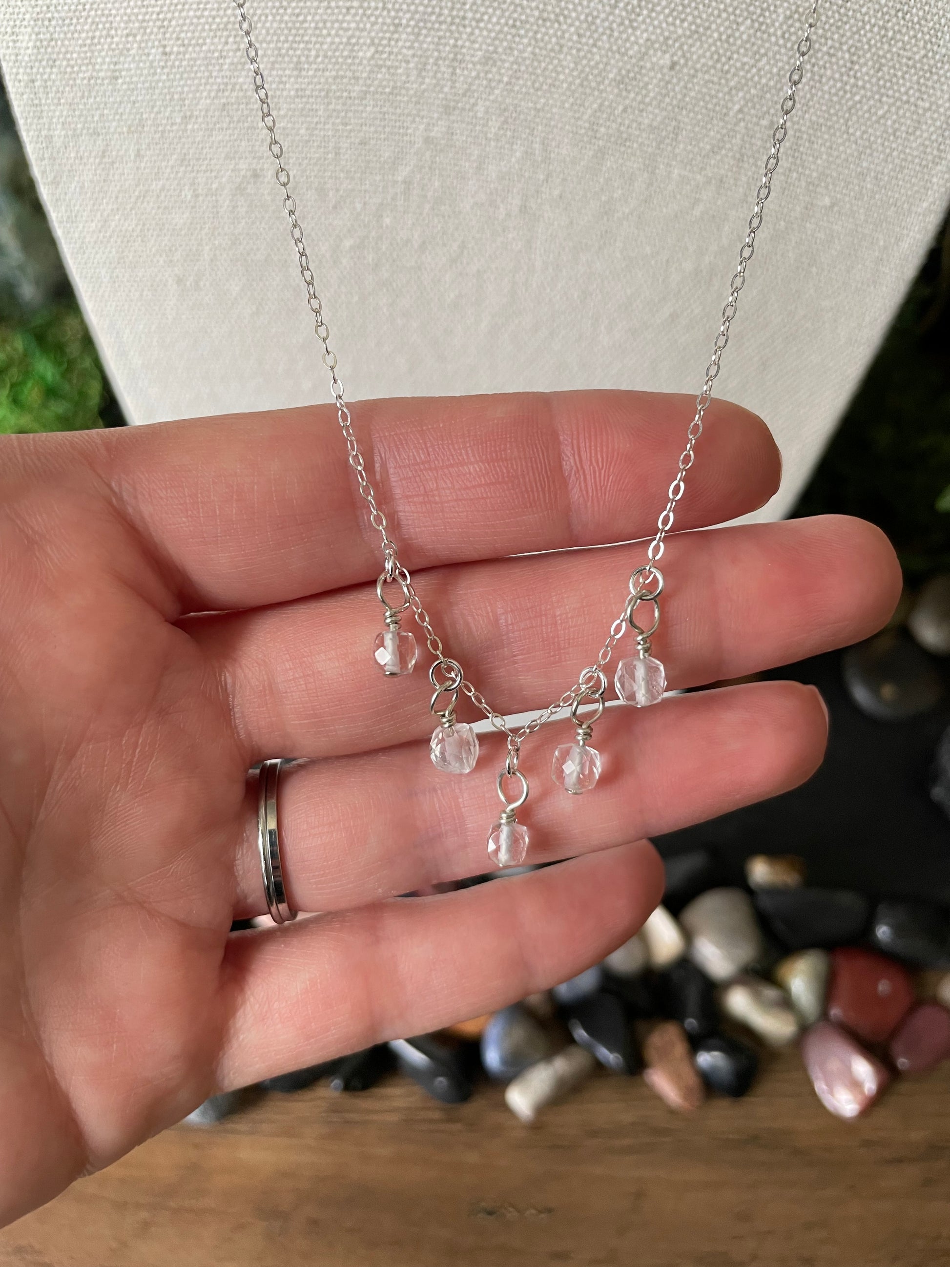 Silver necklace being held by a hand with a background of gemstones