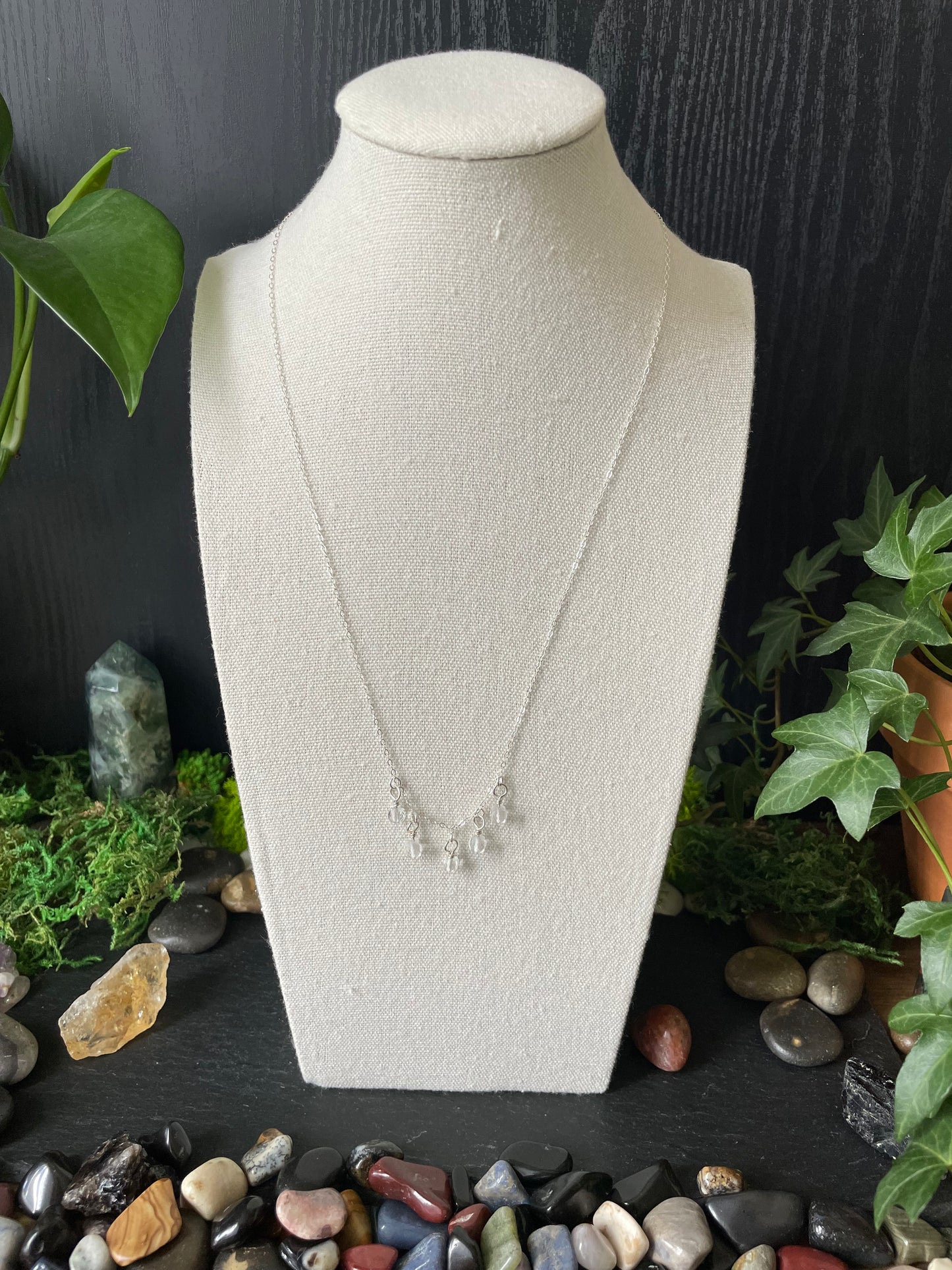 Silver necklace worn on a bust with greenery and stones in the background