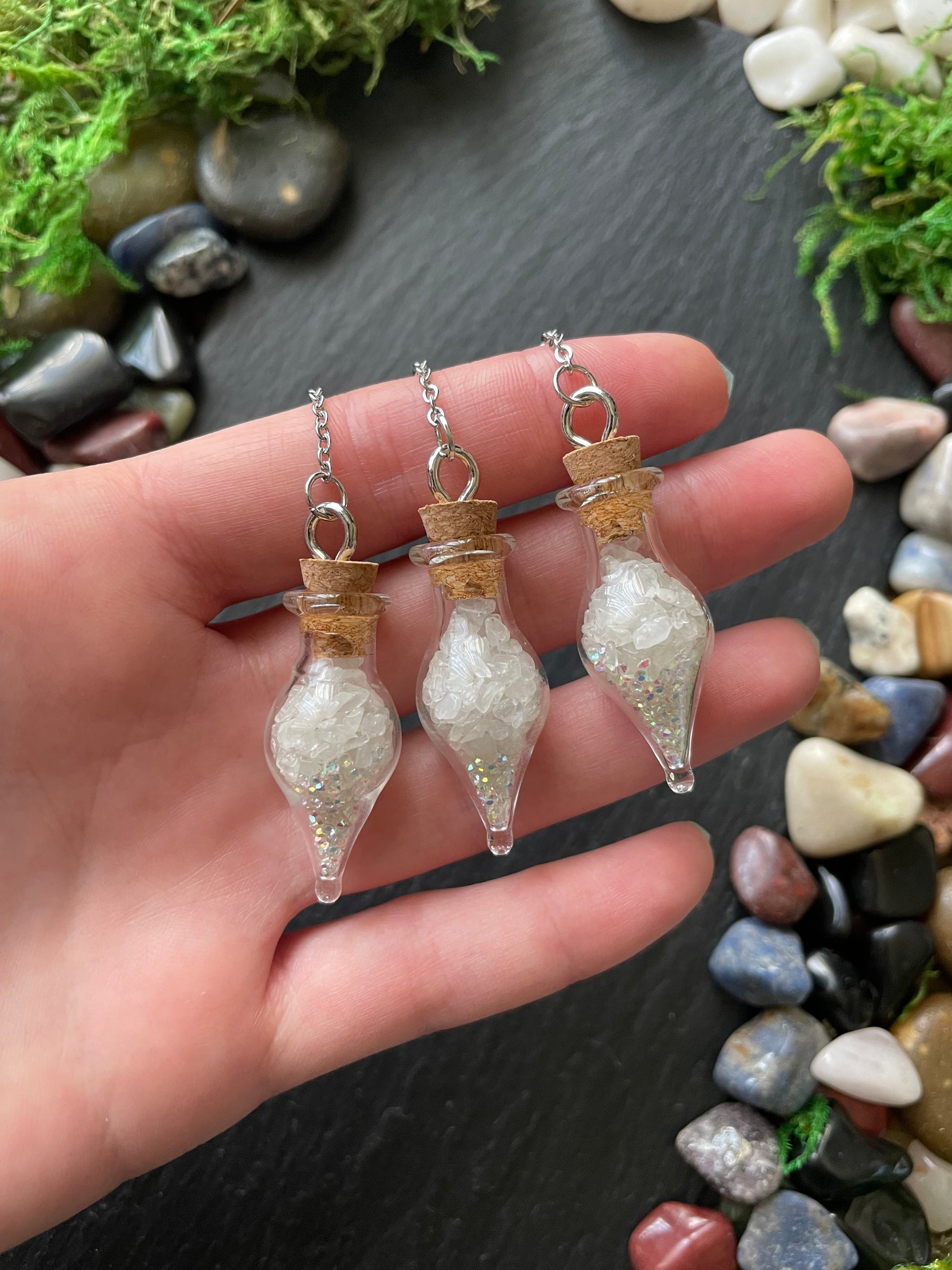 Hand holding three small glass vial charms with a natural stone background
