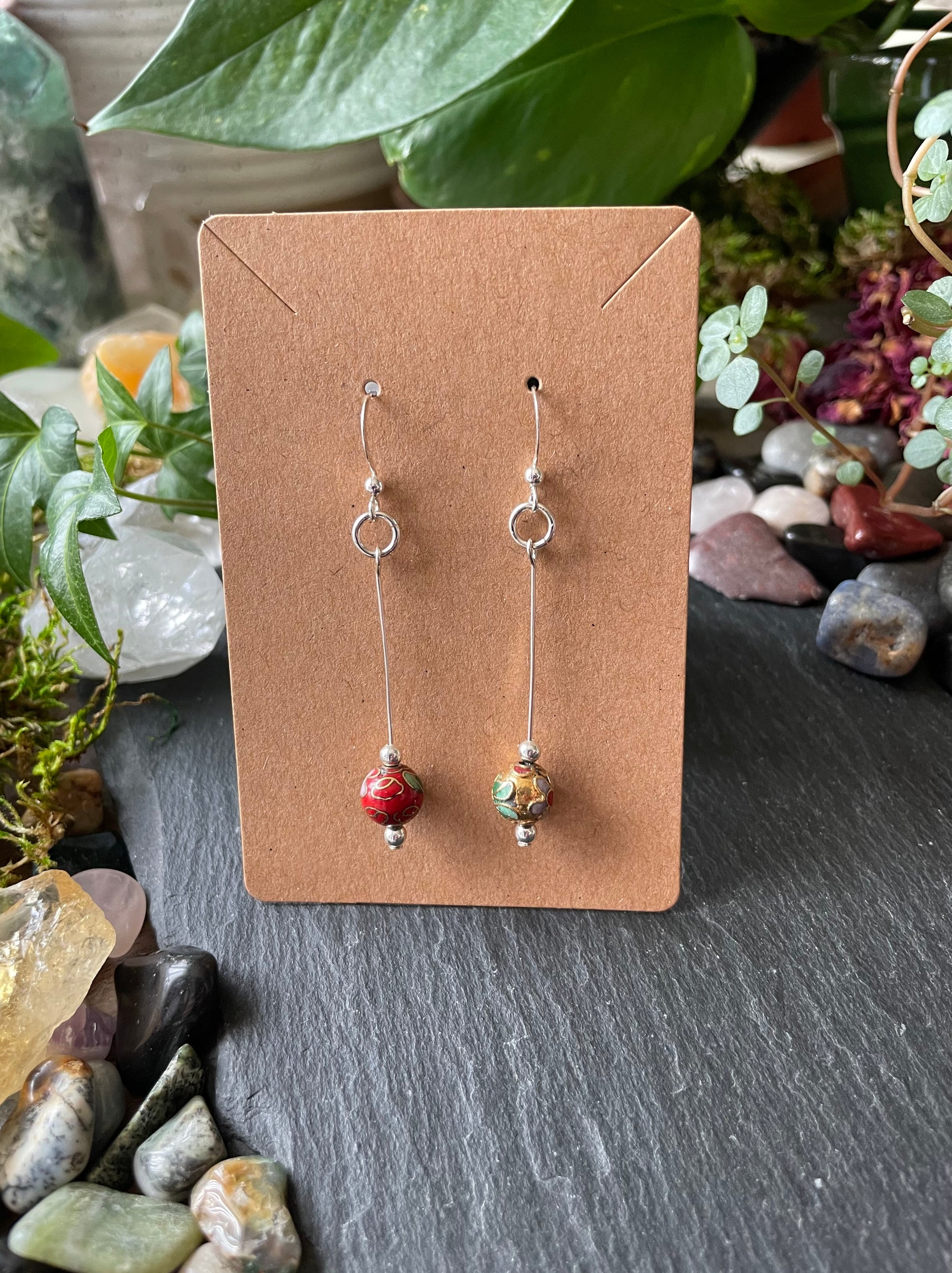 Pair of earrings on a brown card with a natural stone and plant background