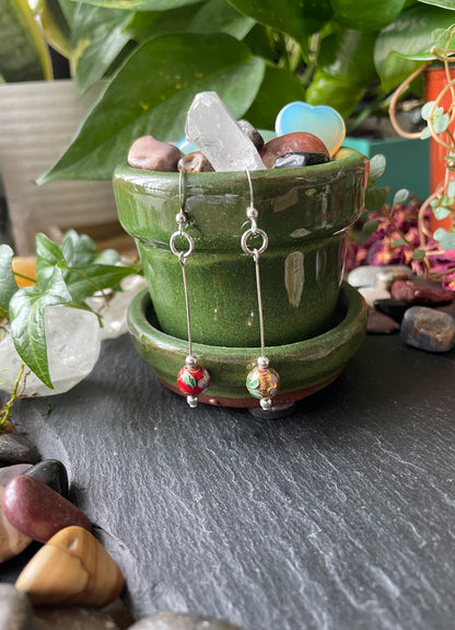 Pair of beaded earrings displayed in a green ceramic pot with decorative stones and crystals.