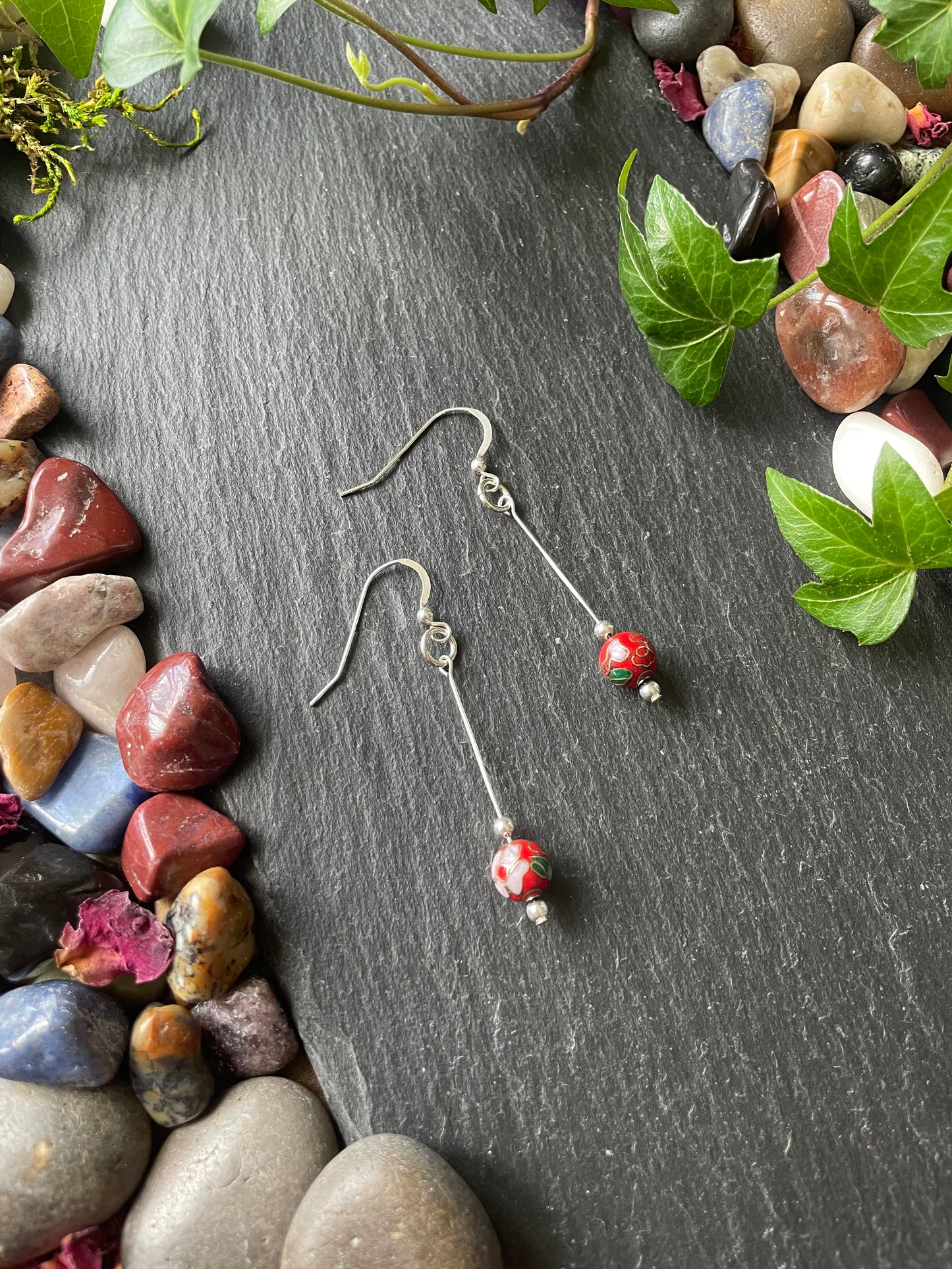 Red flower bead earrings with silver findings on a dark surface with stones and leaves