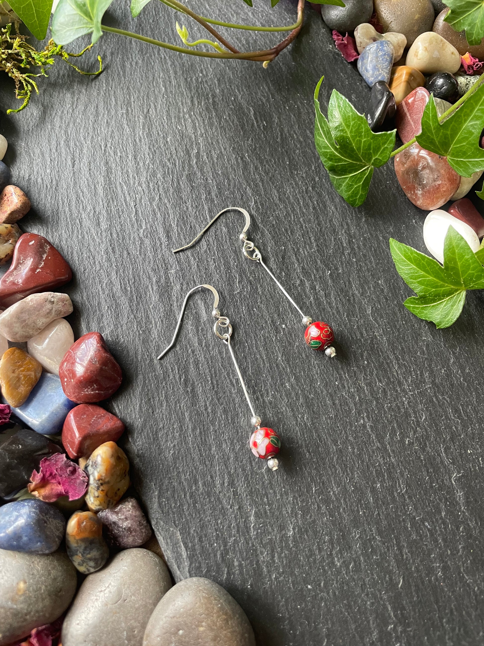Red flower bead earrings with silver findings on a dark surface with stones and leaves