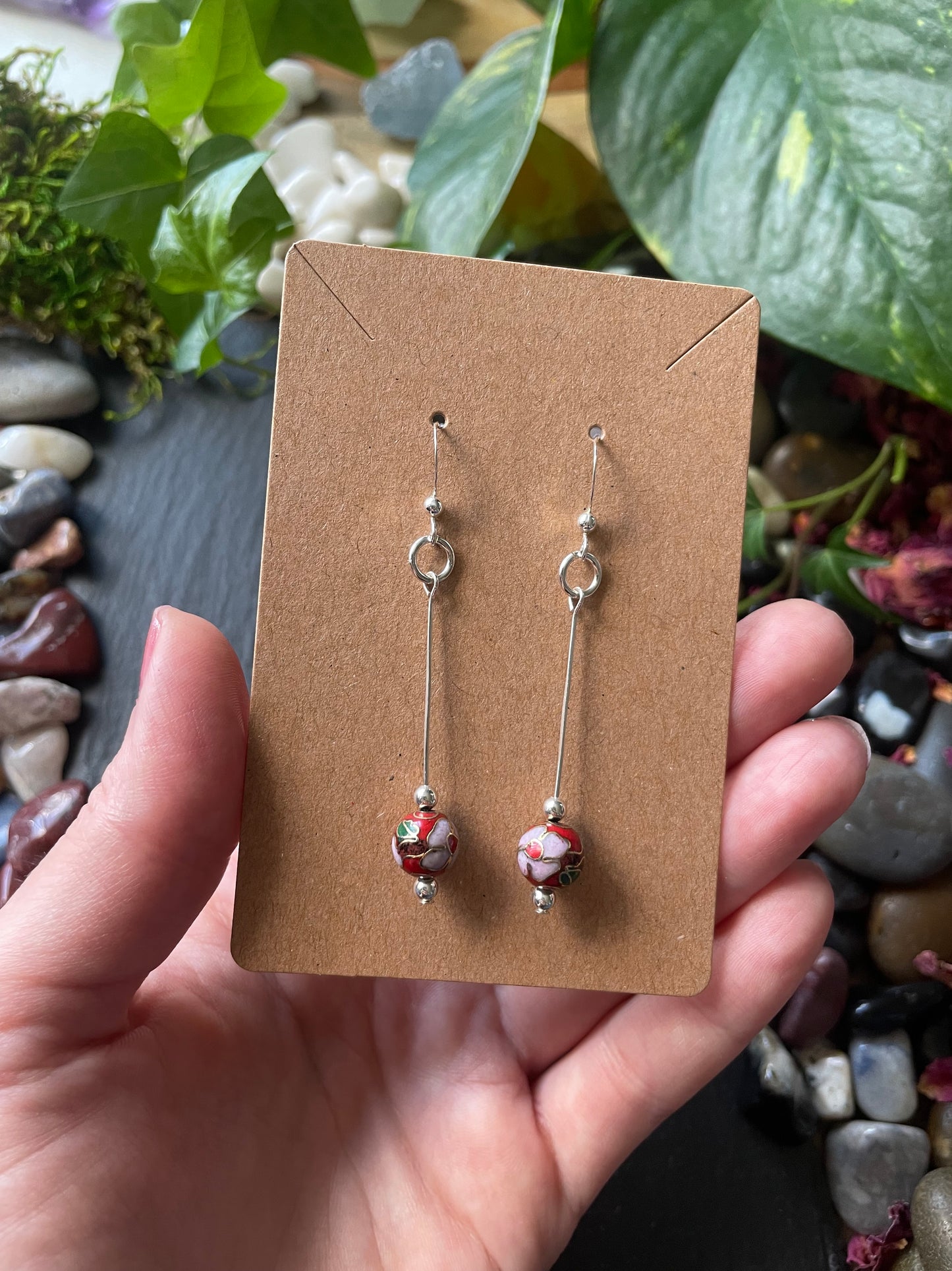 Hand holding a card with red flower bead earrings against a natural background