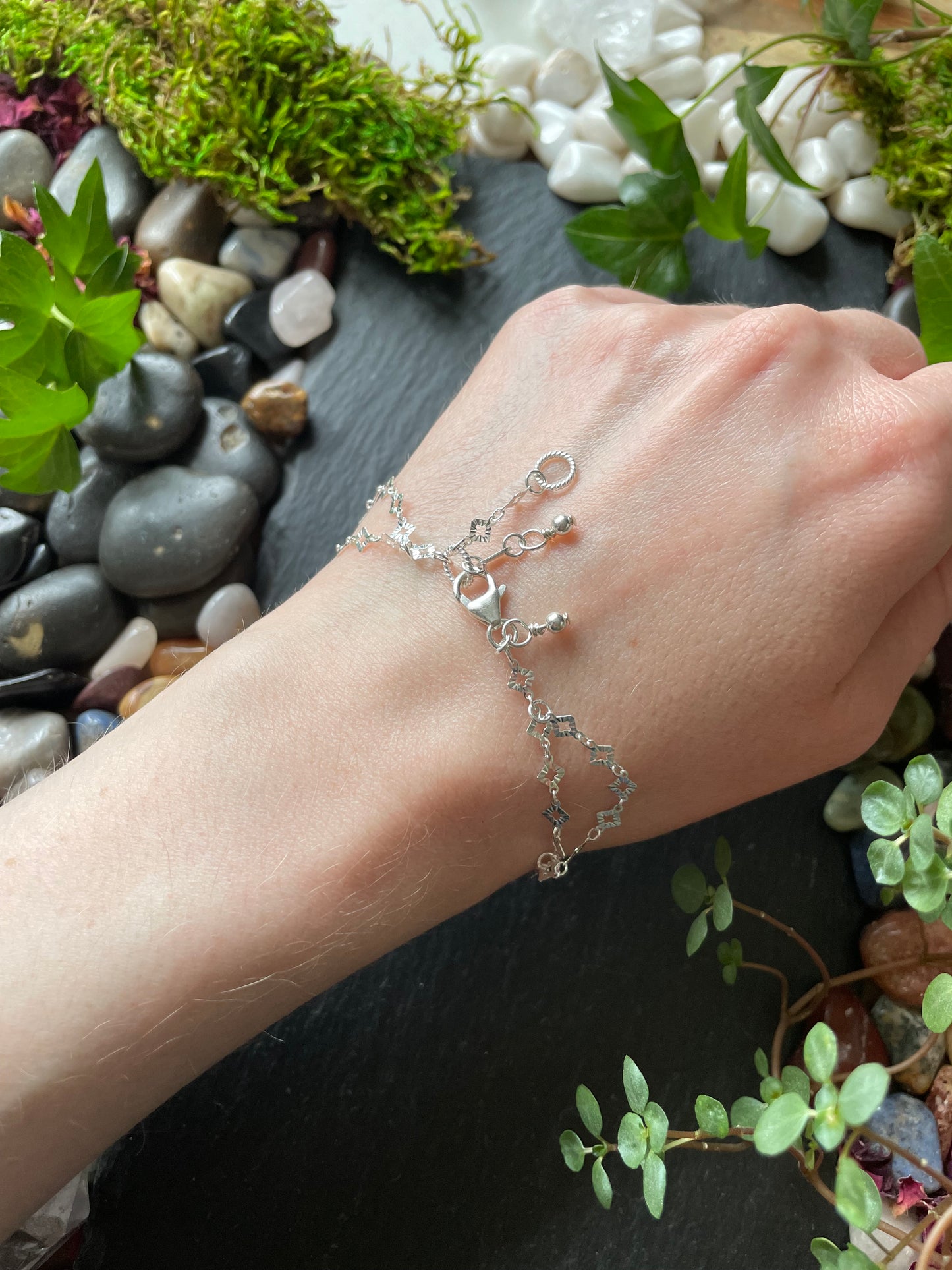 Hand wearing a silver bracelet with a natural background of stones and plants