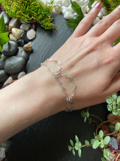 Hand wearing a silver bracelet with a natural background of stones and plants