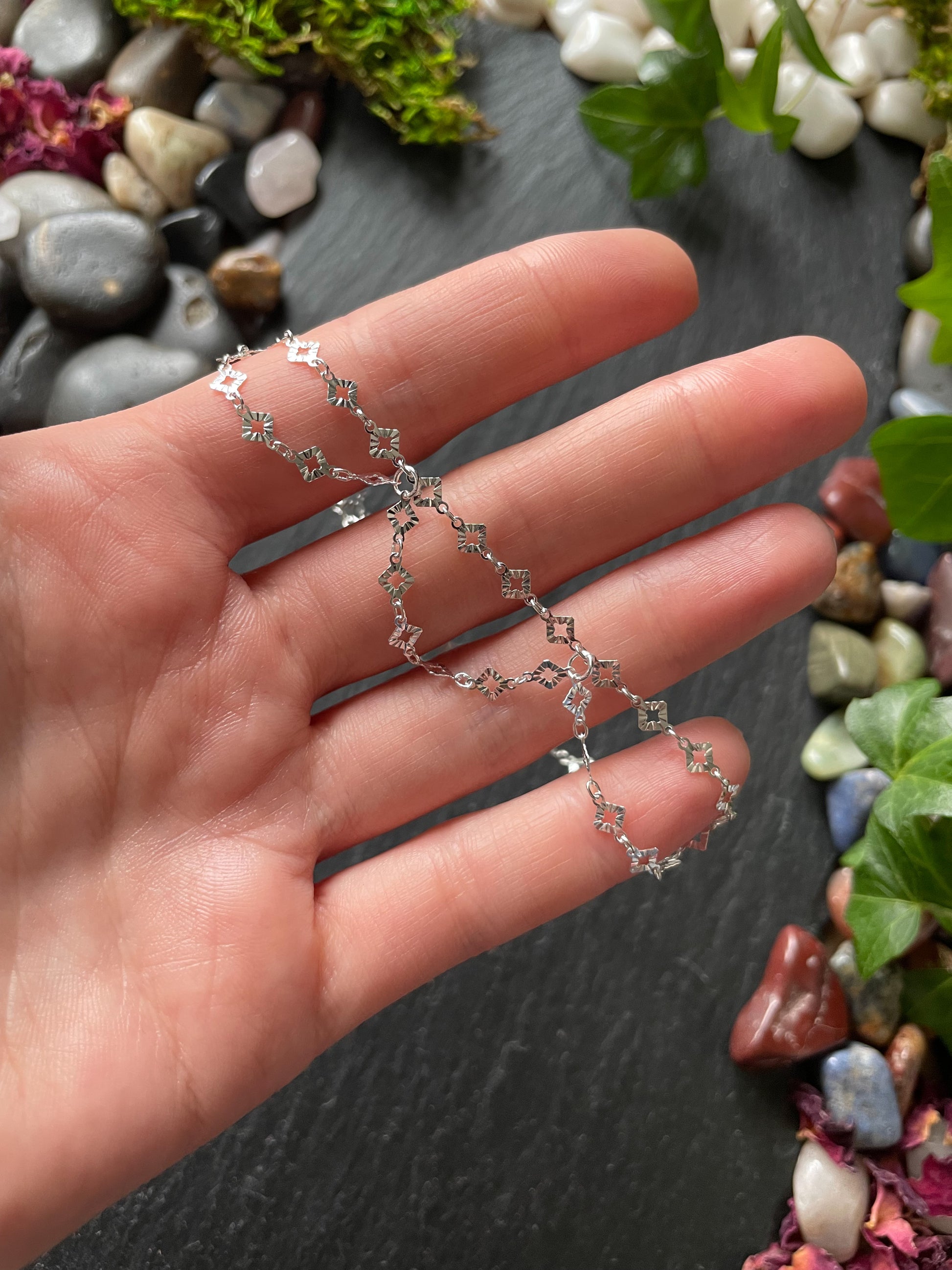 Silver chain necklace held in a hand with a natural stone and plant background