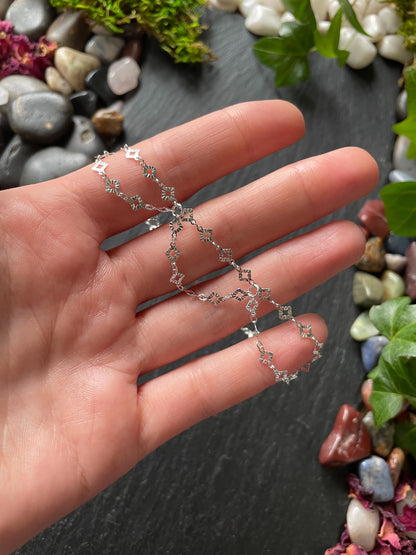 Silver chain necklace held in a hand with a natural stone and plant background