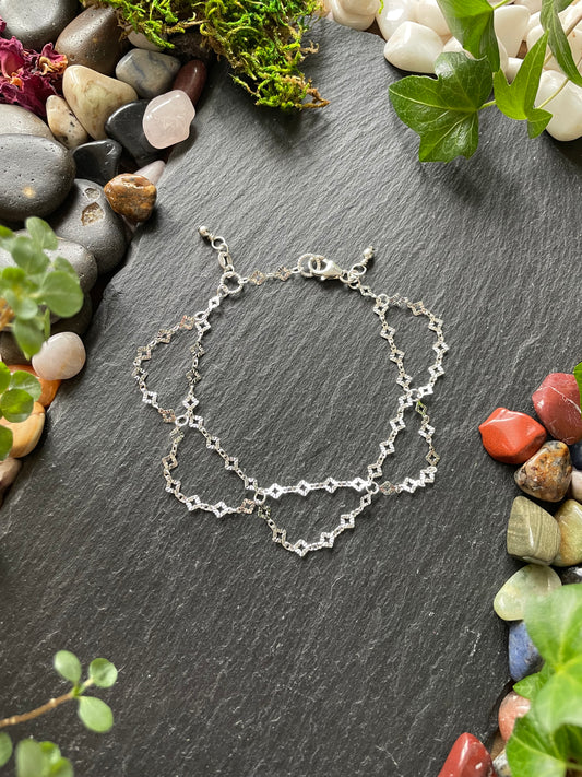Silver chain necklace on a dark stone surface with pebbles and plants