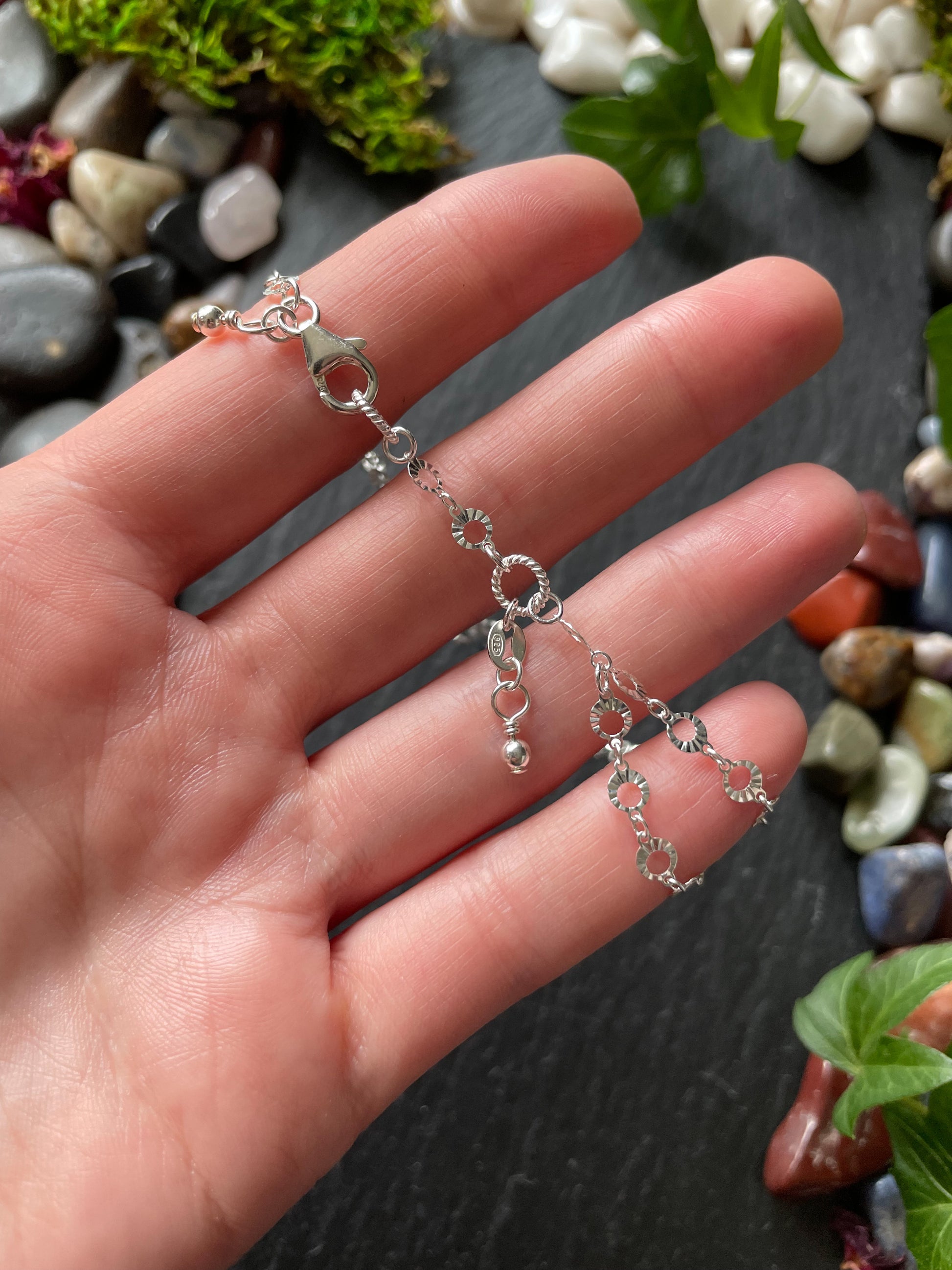 Silver necklace held in a hand with a natural stone background