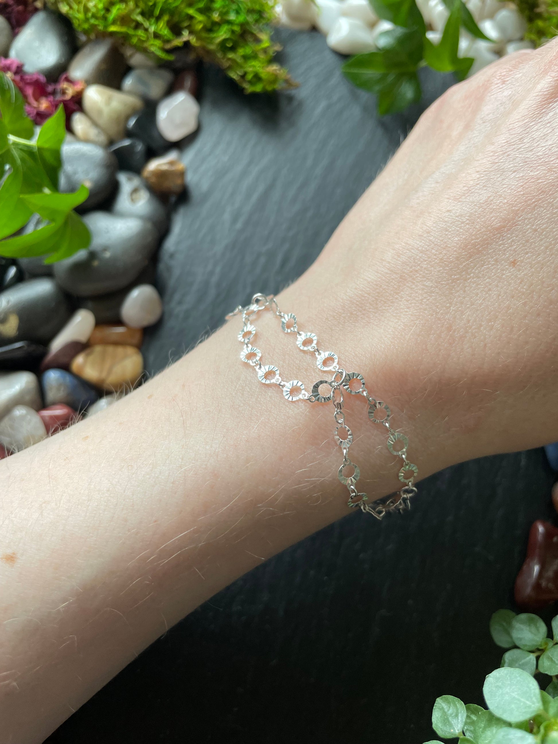 Silver bracelet on a wrist with a natural background of stones and plants