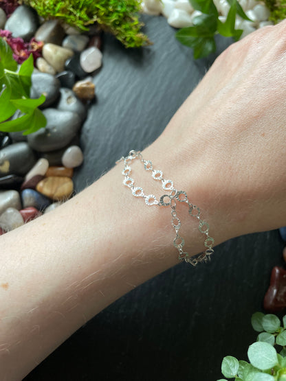 Silver bracelet on a wrist with a natural background of stones and plants