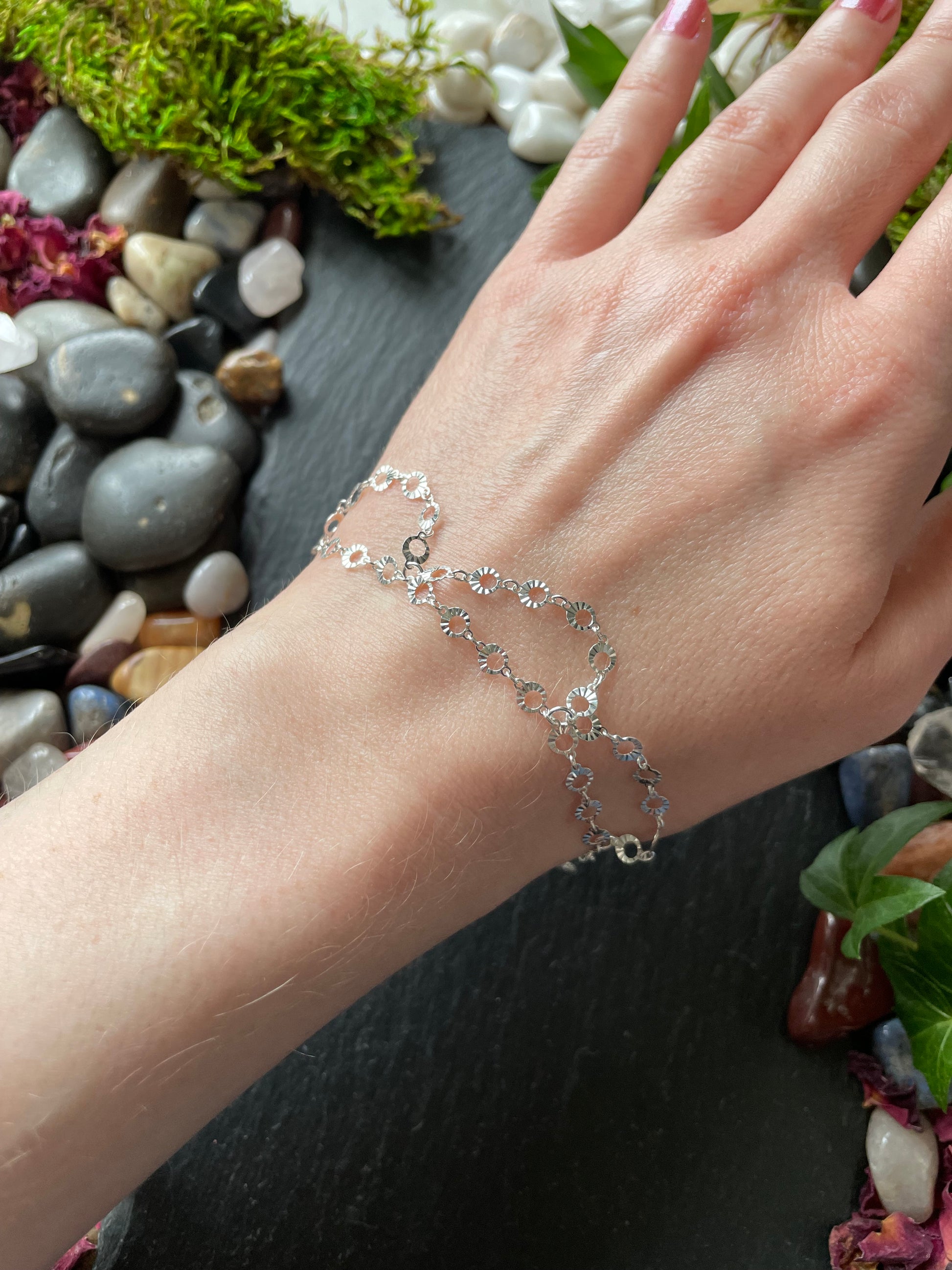 Silver bracelet on a wrist with a natural background of stones and plants