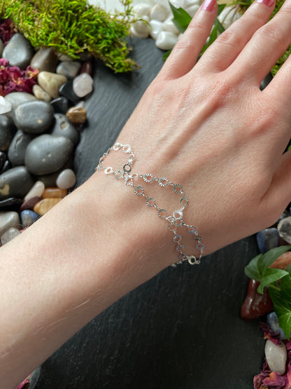 Silver bracelet on a wrist with a natural background of stones and plants