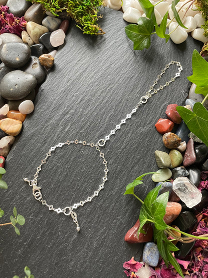 Silver bracelet on a dark stone surface with stones and plants around