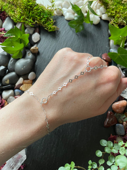 Hand wearing a silver hand chain bracelet with a natural stone and plant background