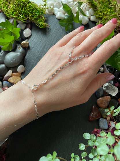 Hand wearing a delicate silver bracelet with a natural stone and plant background