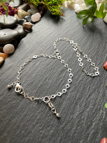 Silver chain bracelet on a dark surface with pebbles and plants in the background