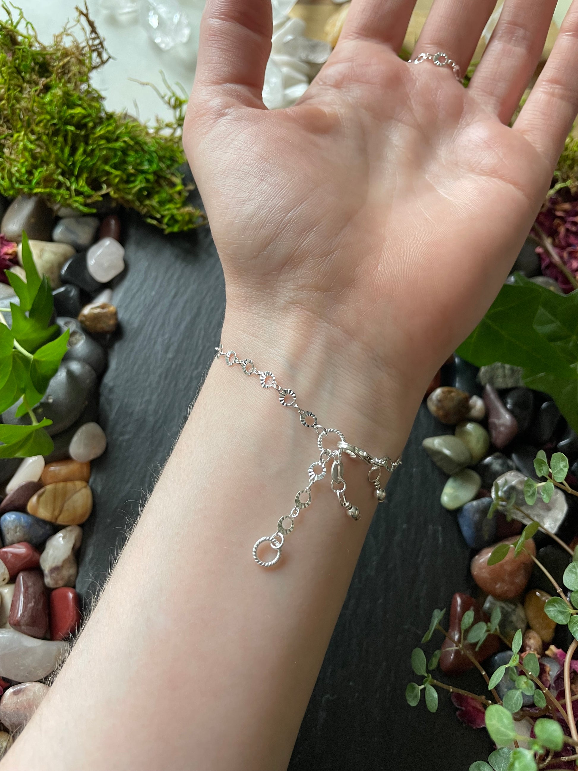 Hand wearing a silver bracelet with a natural background of plants and stones