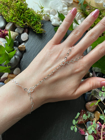 Hand wearing a delicate silver bracelet with a natural background of stones and plants