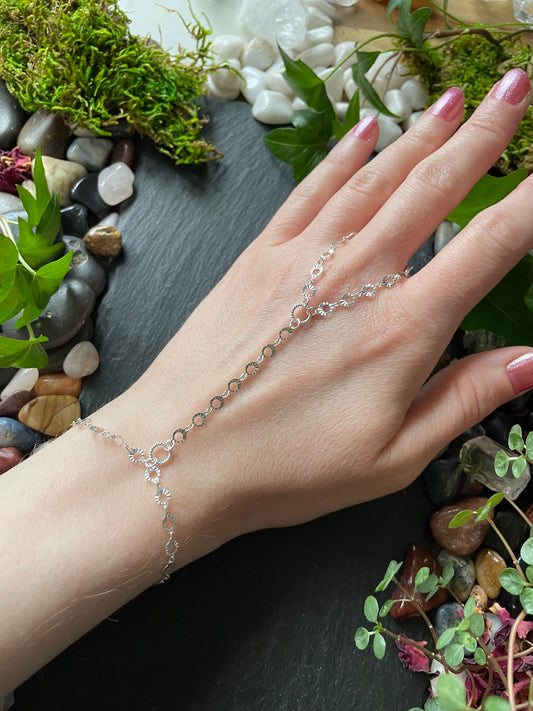 Hand wearing a delicate silver bracelet with a natural stone and moss background
