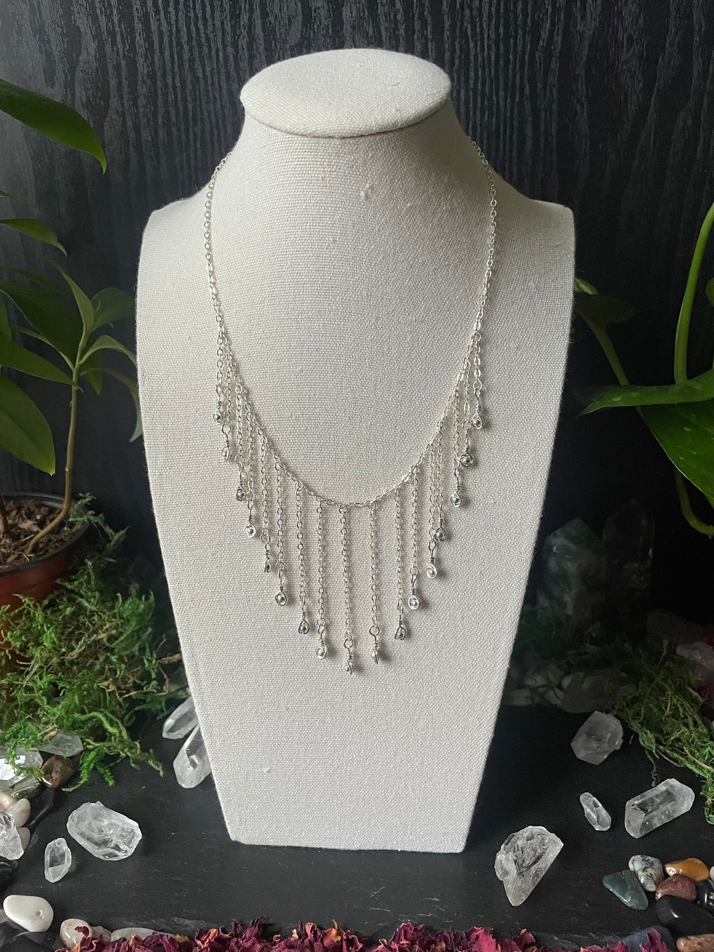 Silver necklace on a white bust with a dark background and decorative elements.
