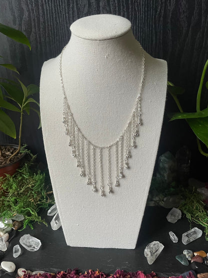 Silver necklace on a white bust with a dark background and decorative elements.