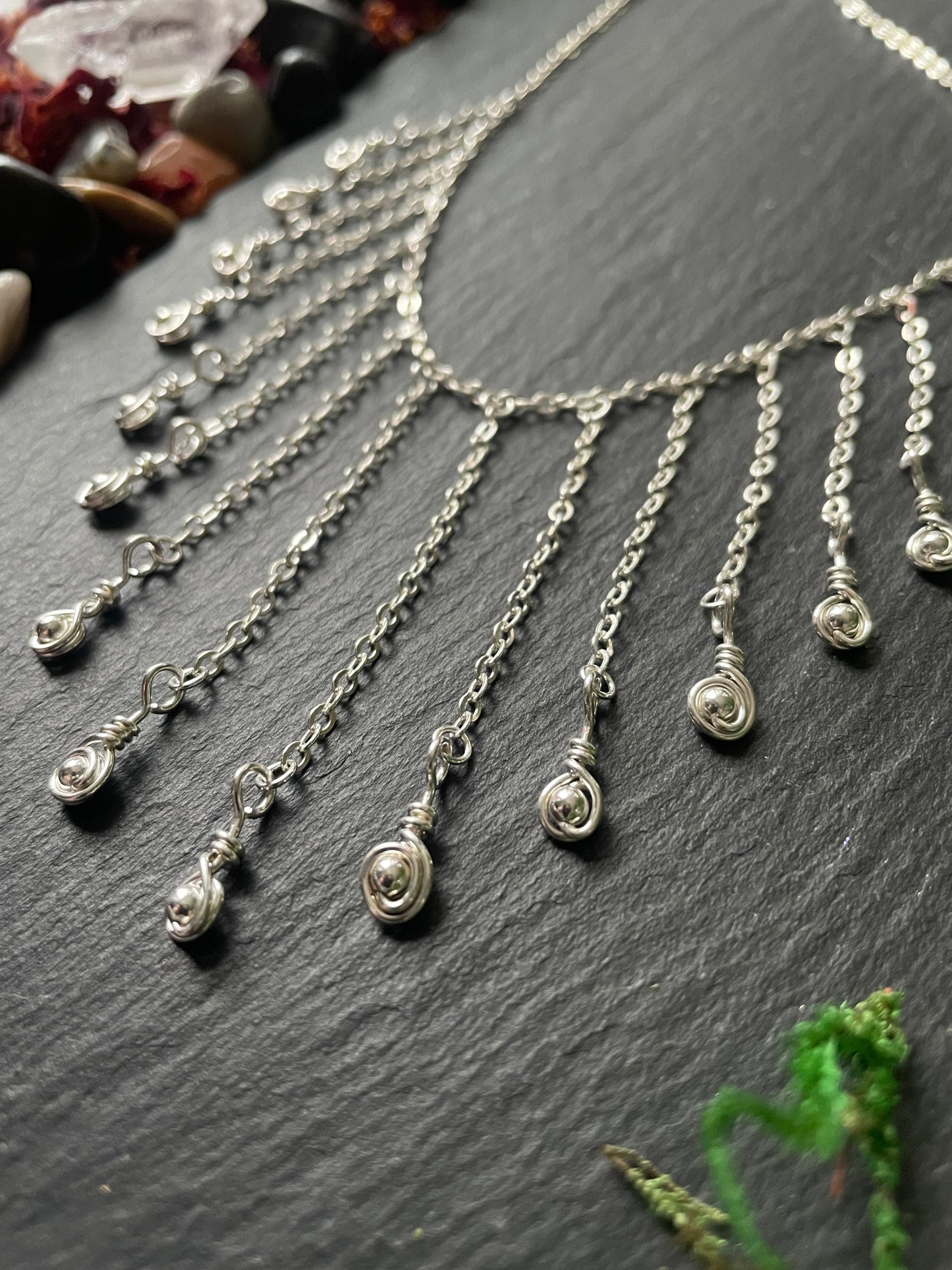 Silver necklace with teardrop charms on a dark surface