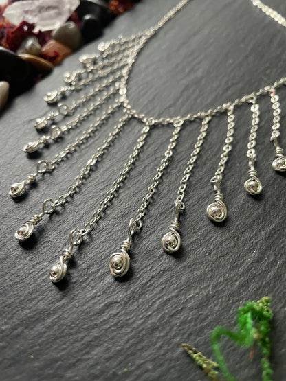 Silver necklace with teardrop charms on a dark surface